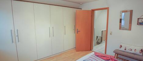 Een slaapkamer met een grote inbouwkast, een bed met gestreepte beddengoed, en een houten deur.
