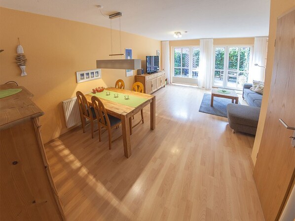 A spacious living area with a wooden dining table, a sofa, and a TV. - Vacation home Jähnert, vacation rental North Sea - Holiday home Jähnert (Varel)