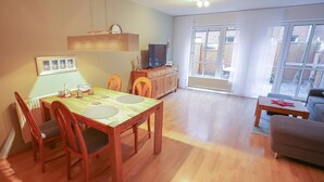 A spacious living area with a wooden dining table and chairs, a sofa, and a television.