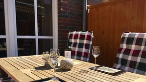 A wooden table with a placemat, two wine glasses, a bottle of wine, a small potted plant, and a tablet displaying a map.