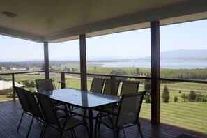 A covered outdoor area with a table and chairs, overlooking a body of water and distant landscape. - Erinvale  Somerset Dam (Hazeldean)