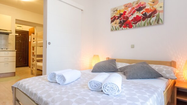 Una cama bien hecha con toallas enrolladas, un cuadro de flores en la pared y una mesita de noche de madera con una lámpara.