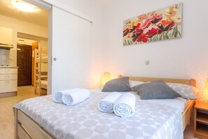 Una cama bien hecha con toallas enrolladas, un cuadro de flores en la pared y una mesita de noche de madera con una lámpara.