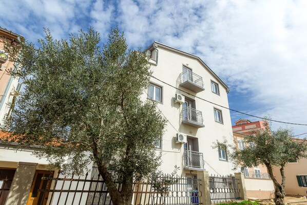 Un edificio de varios pisos con balcones, un acceso con portón y un árbol en la entrada.