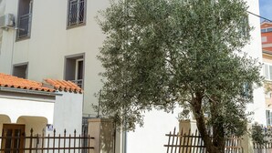 Un edificio de dos pisos con un balcón, un árbol en frente y una cerca de metal.