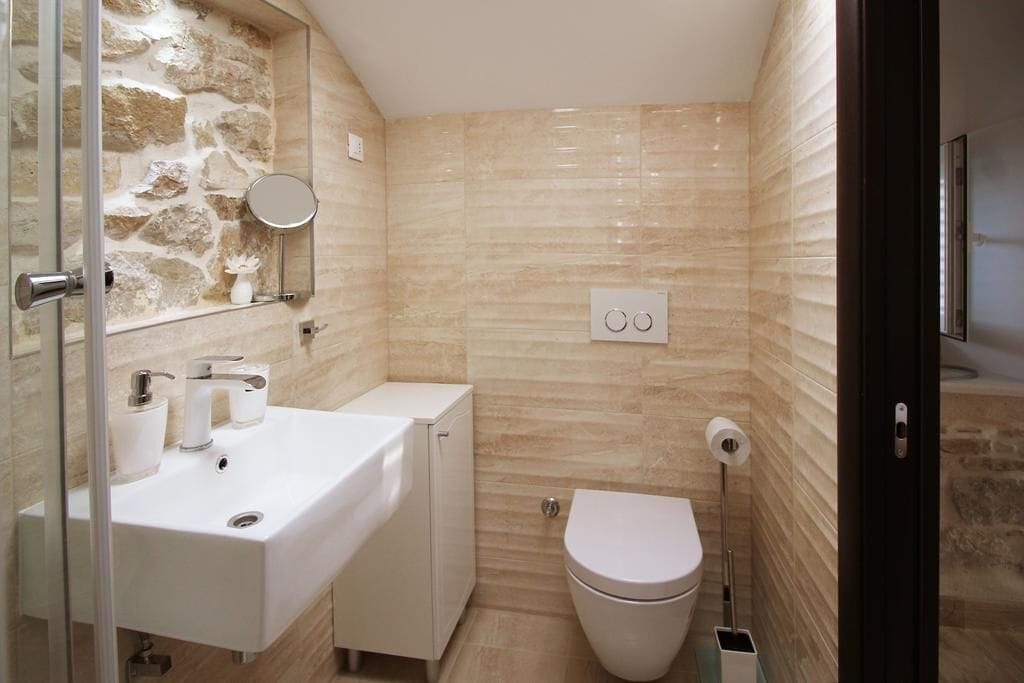 Une salle de bain avec un mur d’accent en pierre, un lavabo blanc, des toilettes et un miroir.