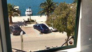 Une vue à travers une fenêtre sur un parking où l’on aperçoit des voitures, un palmier et une étendue d’eau.