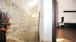 Une pièce avec un mur en pierre, un plancher en bois et un lit avec une table de chevet.