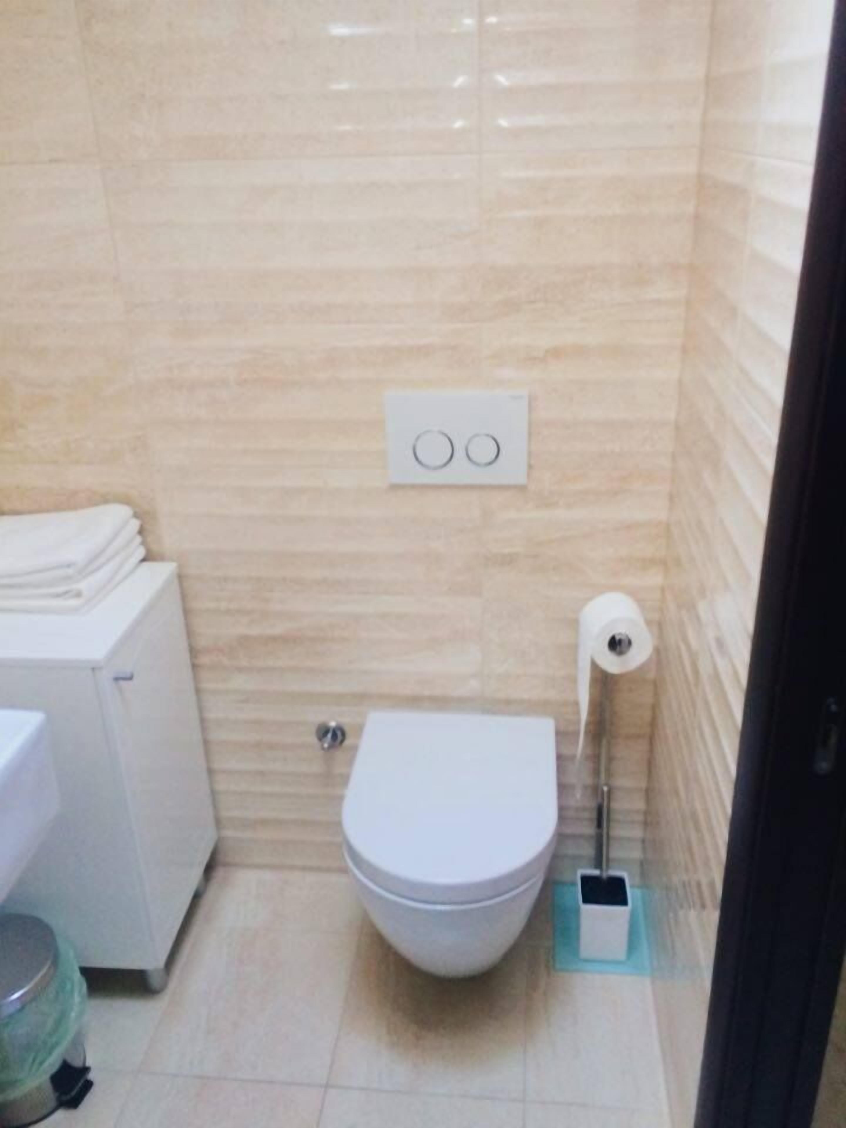 A small, tiled bathroom with a toilet, a stack of white towels, and a toilet paper holder.