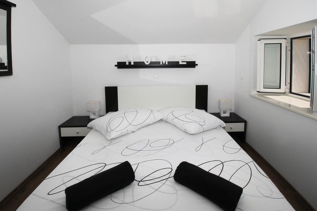 A modern bedroom with a bed, two bedside tables, a nightstand, a window, and a 'HOME' sign on the wall.
