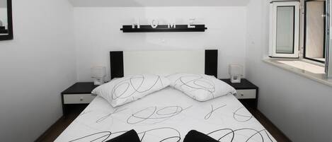 A modern bedroom with a bed, two bedside tables, a nightstand, a window, and a 'HOME' sign on the wall.