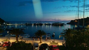 Un port de plaisance au crépuscule, avec des bateaux amarrés, une promenade pavée et des voitures garées.