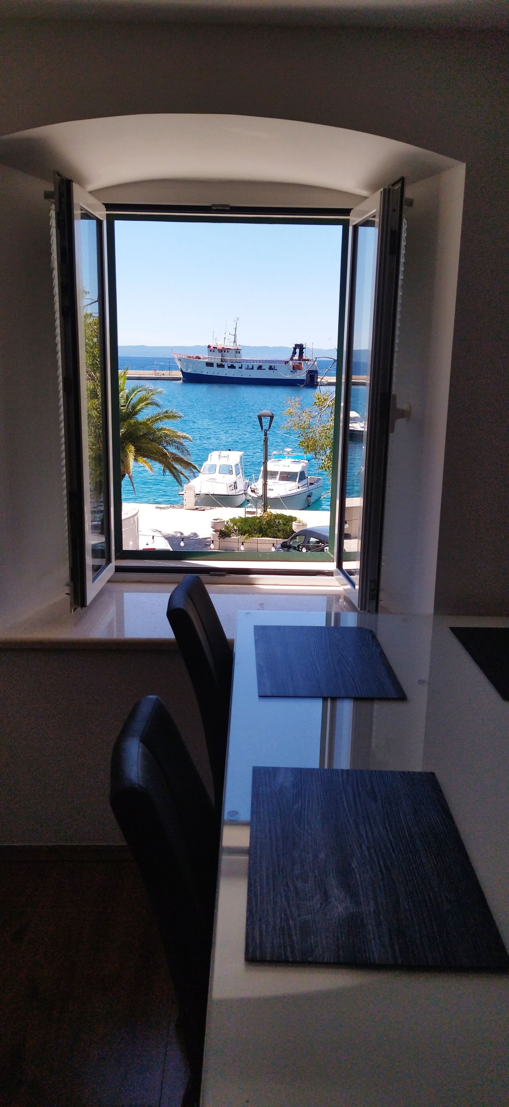A room with a large window overlooking a marina with boats and a ship.