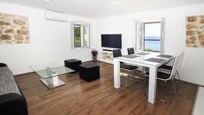 Une pièce moderne et bien éclairée, avec une table à manger en verre, des chaises noires, un canapé et un téléviseur fixé au mur.