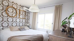 A bedroom with a large bed, a wooden dresser, a hanging lamp, and a window with curtains. - Santa Belgica, Altea (Altea)