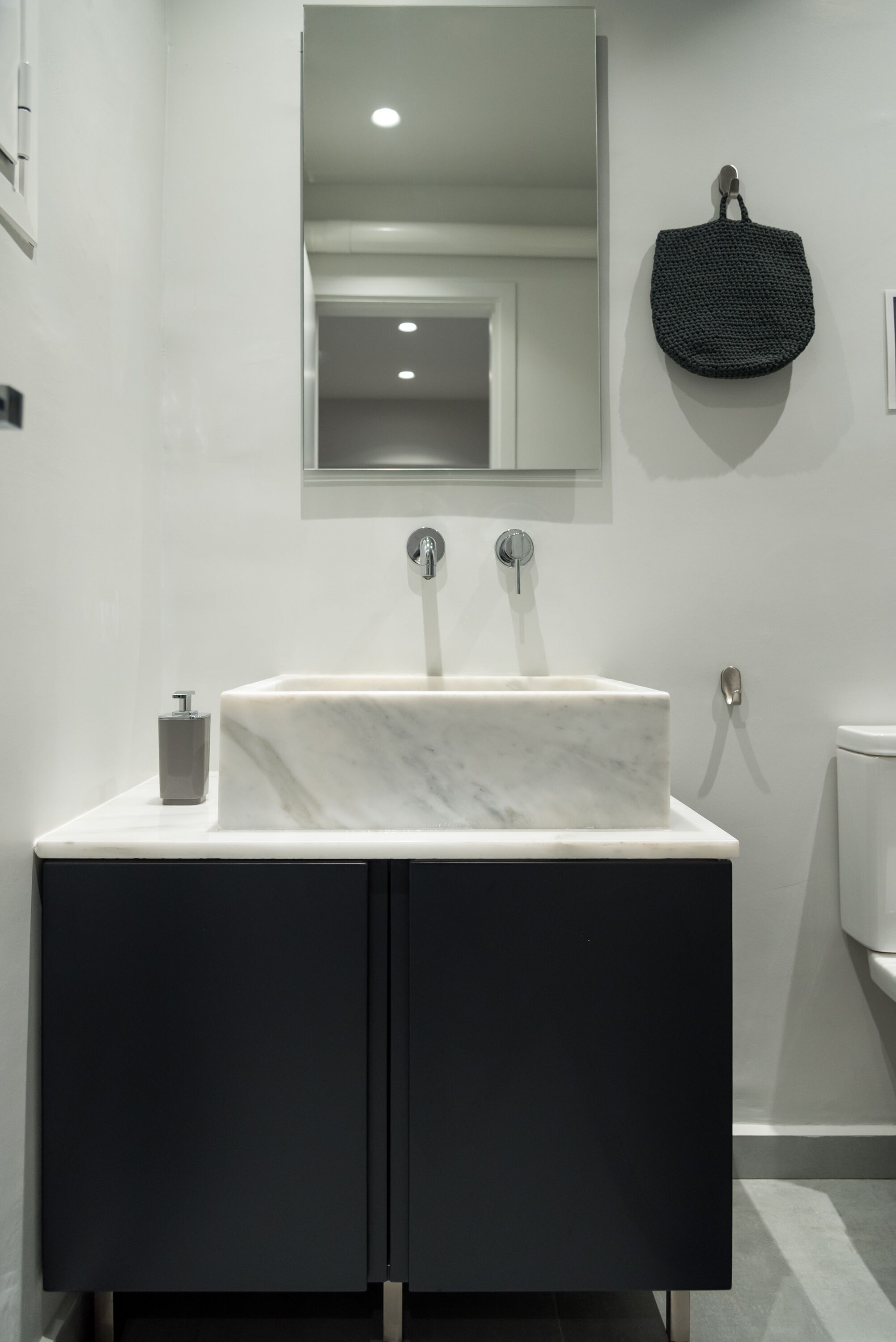Ein modernes Badezimmer mit Marmorwaschbecken, dunklen Schränken, einem wandmontierten Spiegel und einer schwarzen Tasche an der Wand.