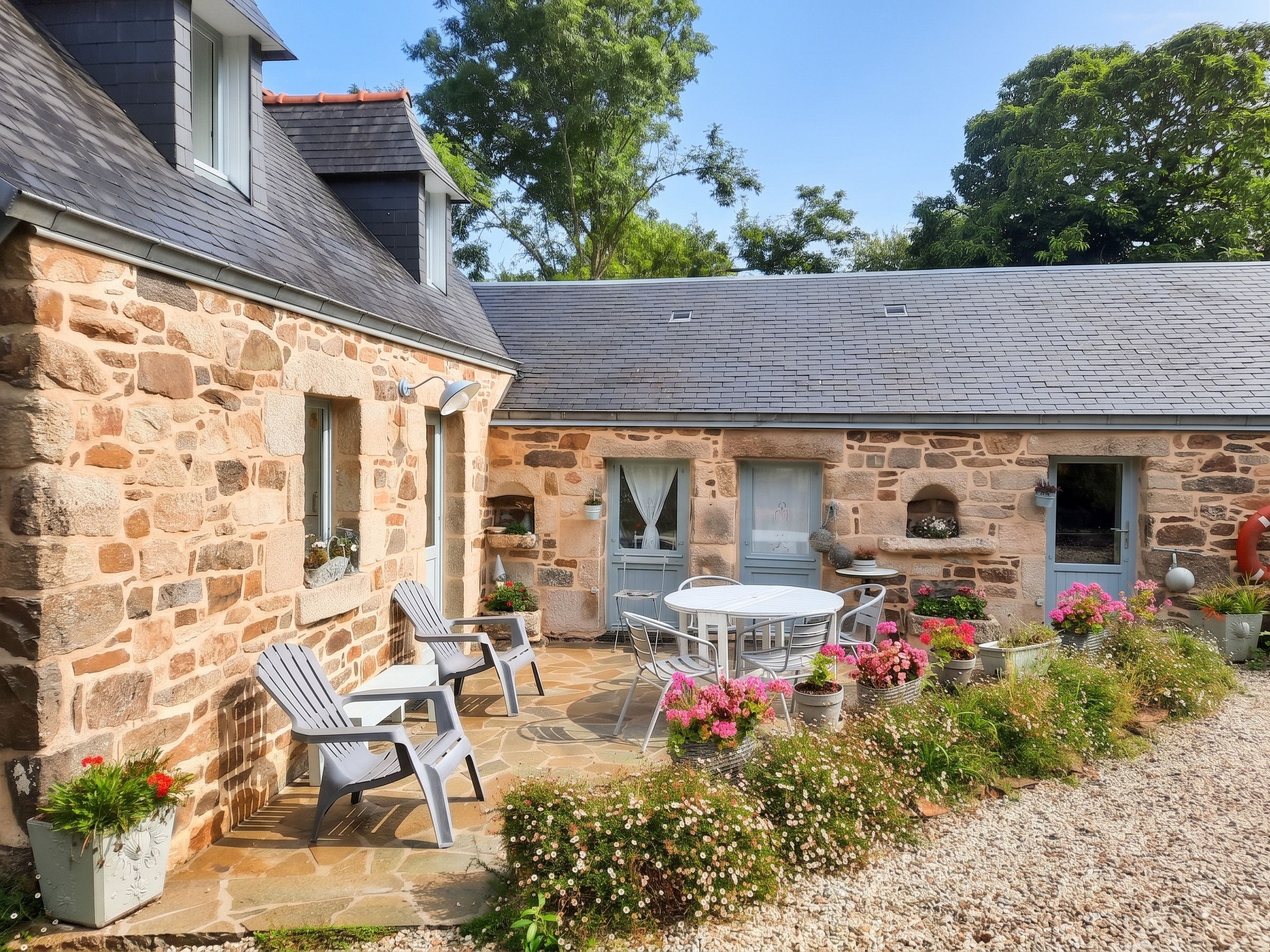 A stone building with a patio area featuring a table and chairs, surrounded by potted plants and flowers.