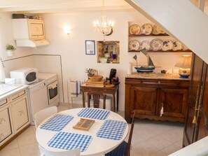 A compact kitchen with a dining area, a chandelier, and a collection of plates on the wall. - Homerez - House in Cléden-Cap-Sizun (Cléden-Cap-Sizun)