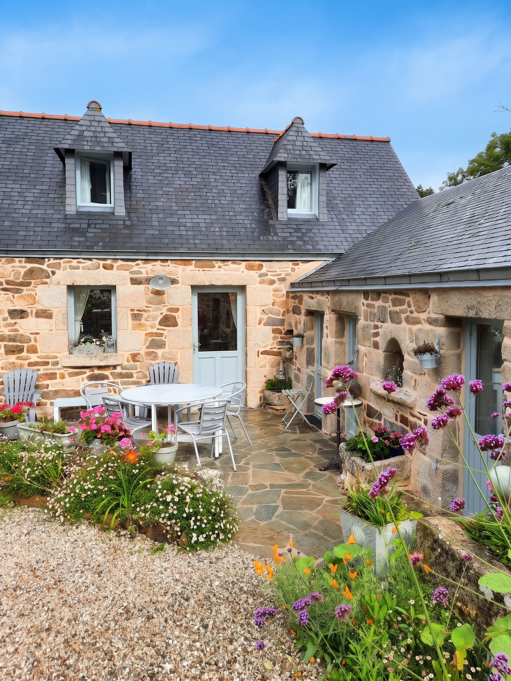 A stone house with a tiled roof, a patio with outdoor furniture, and a garden with various plants and flowers.