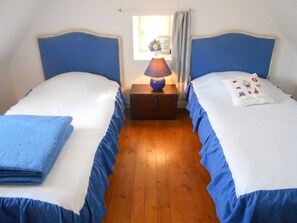 A room with two beds, a nightstand with a lamp, and a window with curtains. - Homerez - House in Cléden-Cap-Sizun (Cléden-Cap-Sizun)