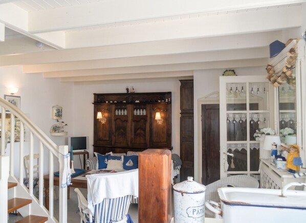 A room with a staircase, a wooden cabinet, a table with striped tablecloth, and a white cabinet with glass doors.