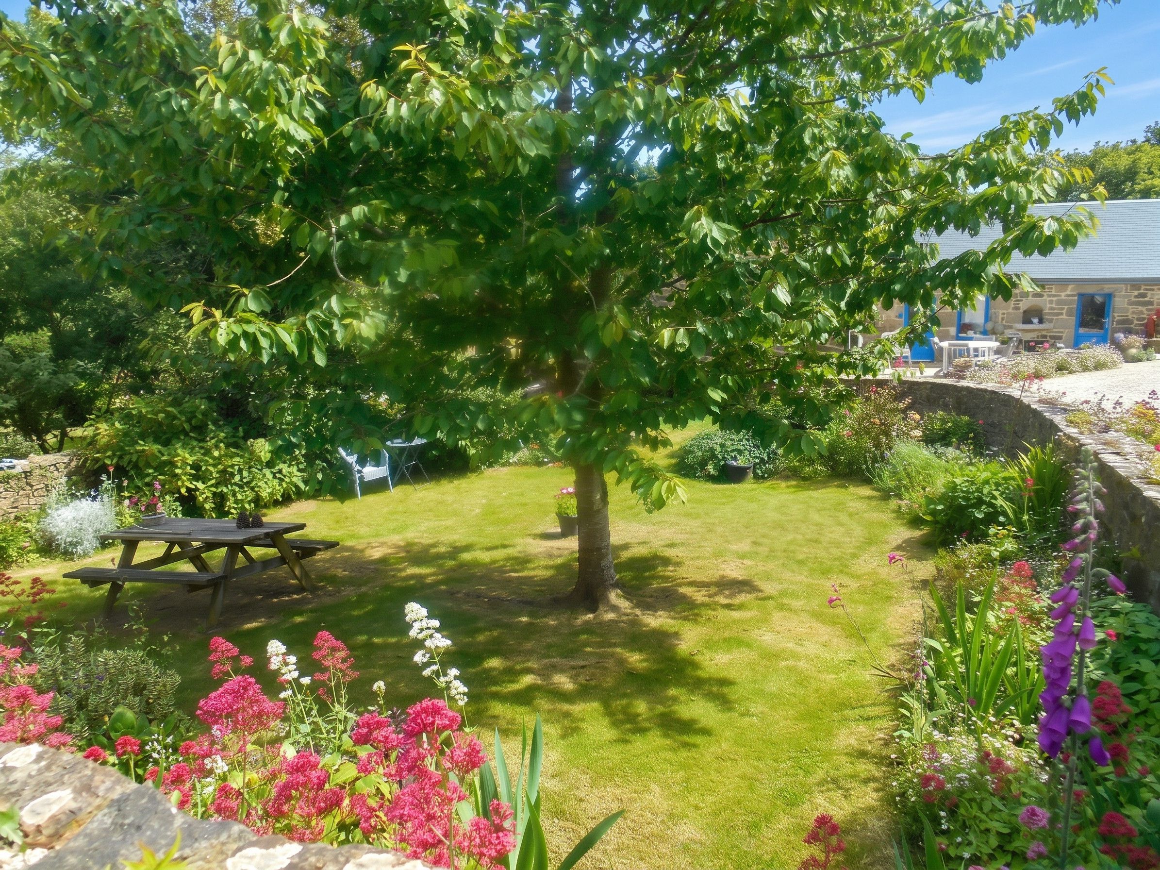 Un giardino curato con un tavolo da picnic, un muro in pietra e diverse piante fiorite.