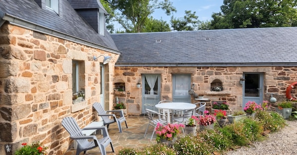 A stone building with a patio area featuring outdoor seating and potted plants. - Homerez - House in Cléden-Cap-Sizun (Cléden-Cap-Sizun)