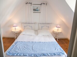 A bedroom with a bed, two bedside tables with lamps, a window with curtains, and a picture on the wall. - Homerez - House in Cléden-Cap-Sizun (Cléden-Cap-Sizun)