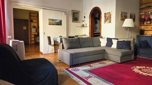 A living room with a grey sectional sofa, a red and white patterned rug, and a dining area with a table and chairs. - Bright apartment in the Center of Rome 70 sqm wifi near Piazza di spagna (Roma)