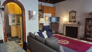 A living room with a sofa, a television, a fireplace, and a kitchen visible through an archway. - Bright apartment in the Center of Rome 70 sqm wifi near Piazza di spagna (Roma)