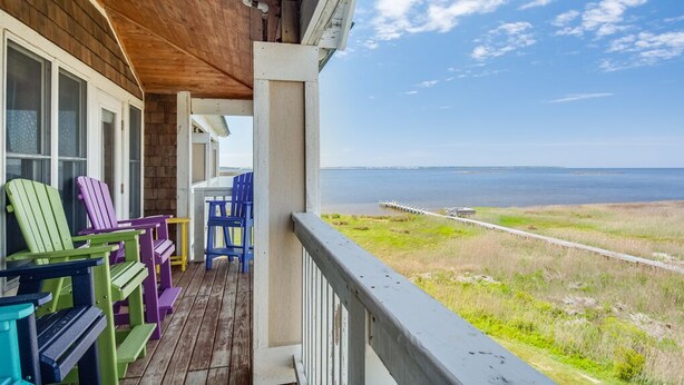A wooden deck with colorful Adirondack chairs, a table, and a view of the ocean. - Look Out: Soundfront Condo, Pool, Great Views! (Nags Head)