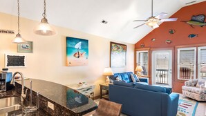 A kitchen with a granite countertop, a sink, and a dining area with a blue sofa and a small table. - Look Out: Soundfront Condo, Pool, Great Views! (Nags Head)