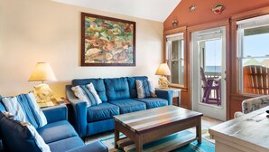 A living room with a blue sofa set, a wooden coffee table, and a colorful fish mural on the wall. - Look Out: Soundfront Condo, Pool, Great Views! (Nags Head)