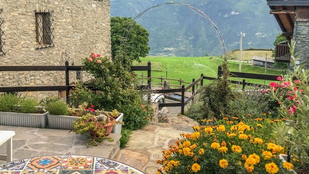 A stone building with a wooden fence, a tiled patio, and a view of green fields and mountains. - Maison Chez Nous by Interhome (Sarre)