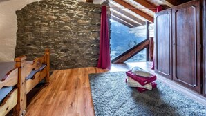 A cozy attic bedroom with a stone wall, wooden beams, a bed, a wardrobe, and a view of the outside. - Maison Chez Nous by Interhome (Sarre)