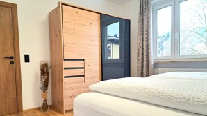 Un dormitorio con un armario de madera, una cama con ropa de cama blanca y una ventana con vistas a árboles.