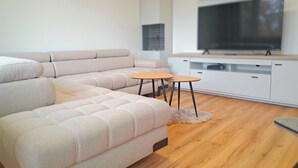 Una sala moderna con un sofá modular, dos mesitas redondas, un televisor de pantalla plana y piso de madera.