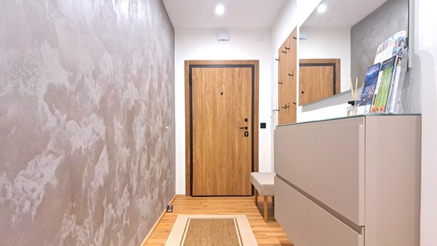 Un pasillo con una puerta de madera, un lavamanos pequeño y un espejo con revistas.