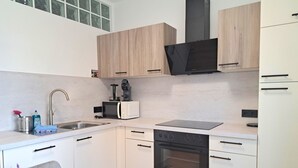 Una cocina moderna con armarios blancos, horno empotrado, microondas y cafetera.