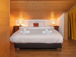 A neatly made bed with white linens and rolled towels, wooden floors, and two bedside lamps.