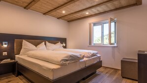 A bedroom with a large bed, wooden ceiling beams, a window with curtains, and a nightstand with a lamp. - Haus Bergsonne by Interhome (Saas-Almagell)