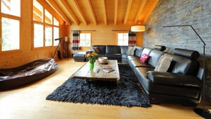 Un salon chaleureux avec un canapé en cuir noir, des poutres en bois et un mur en pierre.