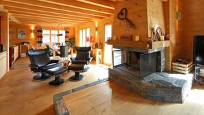Un intérieur spacieux, avec des éléments en bois, une cheminée en pierre, des fauteuils en cuir et un coin repas.
