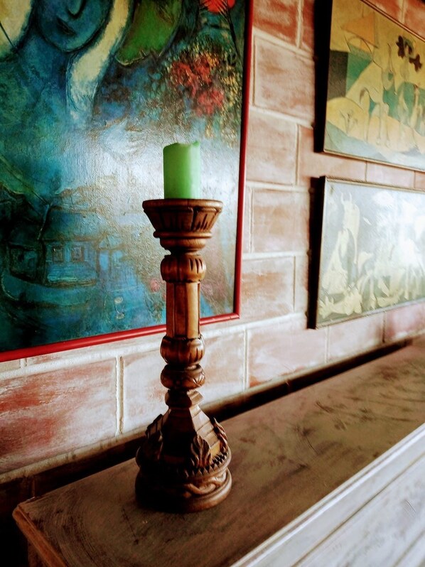 Un candelabro con una vela verde sobre una mesa de madera, frente a una pared con diseños de azulejos y obras de arte.