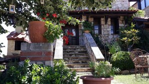 A stone building with a tiled roof, a stone staircase leading to the entrance, and potted plants in the foreground.