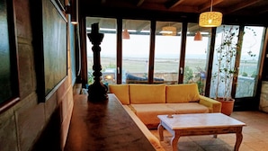 A room with a wooden bench, a yellow sofa, and a small table. There are large windows with a view of the outdoors.