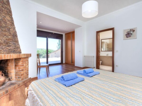 A bedroom with a fireplace, a large bed, a view through a sliding door, and a bathroom visible through an open door.