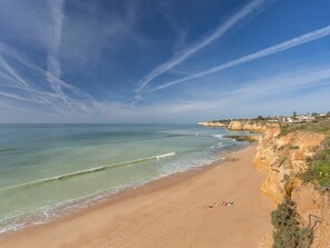 A beach with clear skies, calm waters, and a rocky cliff.