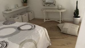 A bedroom with a bed, a small desk, a mirror, and a potted cactus.