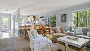 Ein geräumiges Wohnzimmer mit Essbereich, großen Fenstern und Blick auf Grünflächen.